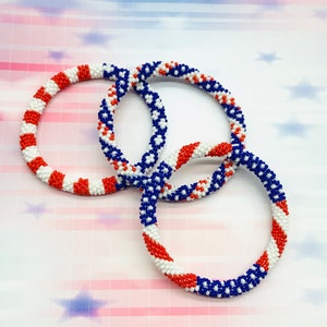 Puede incluir: Tres pulseras de cuentas en rojo, blanco y azul, que se asemejan a la bandera estadounidense. Las pulseras est&aacute;n tejidas juntas en un patr&oacute;n circular.