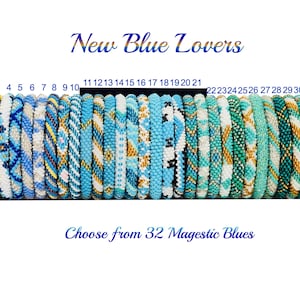 Puede incluir: Una colección de 32 pulseras cilíndricas de cuentas dispuestas en fila sobre un soporte negro. Las pulseras presentan varios patrones en azul, blanco y dorado. El texto en la parte superior dice New Blue Lovers y en la inferior Choose from 32 Magestic Blues.