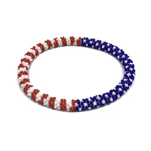 May include: A red, white, and blue beaded bracelet. The beads are arranged in a striped pattern.