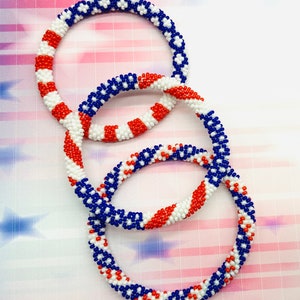 Puede incluir: Tres pulseras de cuentas en colores rojo, blanco y azul. Las pulseras est&aacute;n apiladas una encima de la otra.