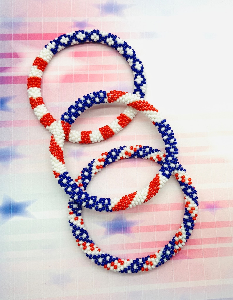 Puede incluir: Tres pulseras de cuentas en colores rojo, blanco y azul. Las pulseras est&aacute;n apiladas una encima de la otra.