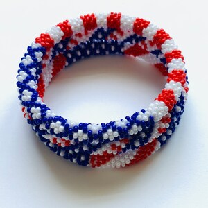 Puede incluir: Un brazalete de cuentas rojas, blancas y azules con un patr&oacute;n tejido. El brazalete est&aacute; hecho de cuentas peque&ntilde;as y tiene un di&aacute;metro de aproximadamente 5 cm.