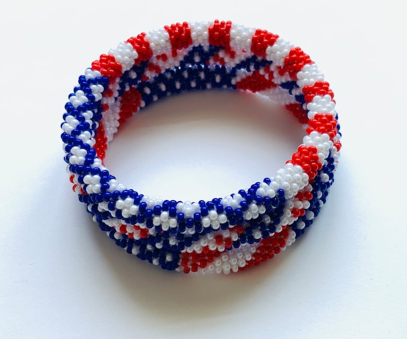 Puede incluir: Un brazalete de cuentas rojas, blancas y azules con un patr&oacute;n tejido. El brazalete est&aacute; hecho de cuentas peque&ntilde;as y tiene un di&aacute;metro de aproximadamente 5 cm.