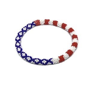 May include: A white, red, and blue beaded bracelet with a patterned design. The bracelet is made of small beads and is stretchy.