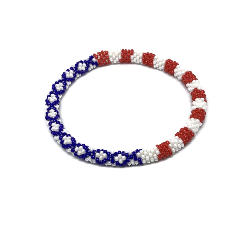 May include: A white, red, and blue beaded bracelet with a patterned design. The bracelet is made of small beads and is stretchy.