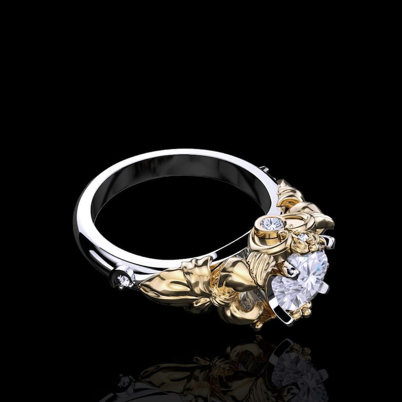 Puede incluir: Un anillo de plata y oro con un gran diamante de forma de coraz&oacute;n transparente y diamantes m&aacute;s peque&ntilde;os en la banda. El anillo tiene un dise&ntilde;o floral con detalles intrincados.