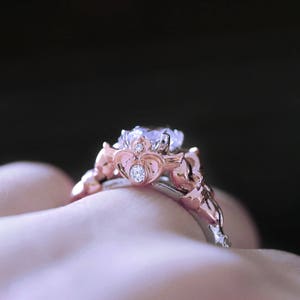Puede incluir: Un anillo de compromiso de oro rosa con una piedra central grande y transparente y piedras de acento m&aacute;s peque&ntilde;as. El anillo est&aacute; engastado en un dise&ntilde;o delicado e intrincado.
