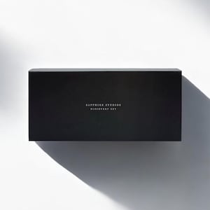 以下が含まれることがあります： 明るい色の「SAPPHIRE STUDIOS DISCOVERY SET」というテキストが入った長方形の黒い箱。白い背景に箱が中央に配置され、影ができています。