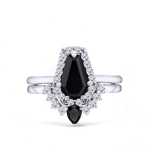 Può includere: Un set di anelli in argento con una pietra centrale nera a forma di bara, circondata da un alone di piccole pietre trasparenti. Una fascia abbinata e una pietra nera a forma di goccia completano il design.