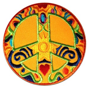 Op de afbeelding: Geborduurde ronde patch met een vredesteken in oranje, met een gele zonnestraal in het midden. Het ontwerp bevat een rood hart, blauwe krullen en kleurrijke bloemaccenten. De patch heeft een getextureerd uiterlijk.
