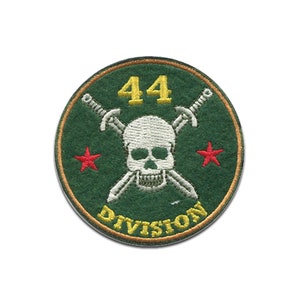 Peut inclure: Un écusson circulaire vert avec une tête de mort blanche et des os croisés, deux étoiles rouges et le texte "44 DIVISION" en jaune.