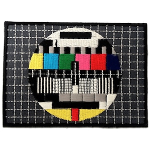 May include: Embroidered patch featuring a classic TV test pattern with a black and white grid, a circle of coloured bars, and a black and white striped pattern.
