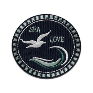 Può includere: Una toppa rotonda ricamata di colore blu navy con un gabbiano bianco e onde. Il testo "SEA LOVE" è ricamato in bianco.
