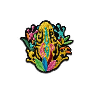 Op de afbeelding: Geborduurde patch met een kleurrijk kikkerontwerp en de tekst "YOUR TRIP". De patch heeft een zwarte rand en bevat gele, roze, blauwe, groene en oranje details. Het kikkerontwerp is omgeven door bladeren en andere decoratieve elementen.