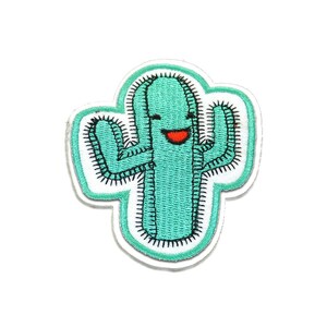Puede incluir: Un parche de cactus turquesa con una cara sonriente y costuras negras. El parche tiene un borde blanco con un contorno turquesa. El cactus tiene una boca roja y está sonriendo.