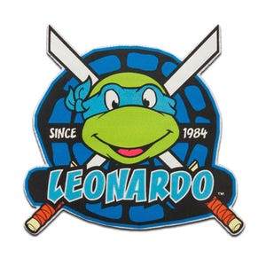 May include: A colourful patch featuring Leonardo from Teenage Mutant Ninja Turtles. The design includes Leonardo's face, a blue mask, and crossed swords. The text "LEONARDO" and "SINCE 1984" are also present.