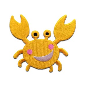 Op de afbeelding: Geborduurde patch met een lachende cartoonkrab. De krab is voornamelijk geel met zwarte ogen, roze wangen en een witte glimlach. De patch heeft een getextureerd uiterlijk en is ontworpen om op stof te strijken of te naaien.