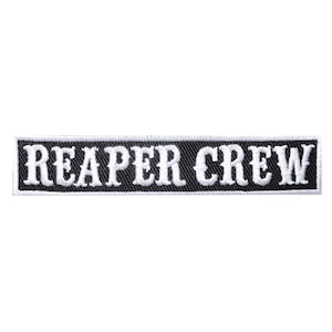Op de afbeelding: Een rechthoekige zwart-witte geborduurde patch met de woorden "REAPER CREW" in vetgedrukte, witte, gestileerde letters. De patch heeft een zwarte achtergrond met een getextureerd uiterlijk en een witte rand.