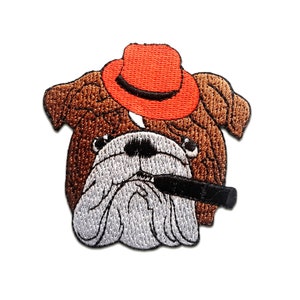 Könnte beinhalten: Gestickter Aufnäher mit einem Bulldoggen-Motiv, die einen orangefarbenen Hut trägt und eine schwarze Zigarre raucht. Der Bulldogge hat braunes Fell, eine weiße Schnauze und ist vor weißem Hintergrund dargestellt.