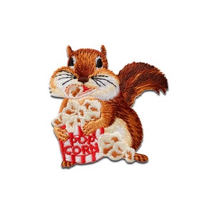 May include: Embroidered patch of a brown squirrel holding a red and white striped bucket of popcorn. The bucket says "POP CORN" in red letters.