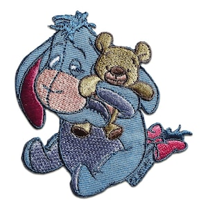 May include: Embroidered patch depicting Eeyore, a blue donkey, embracing a small teddy bear. The patch showcases a detailed design with shades of blue, pink, and brown. Suitable for application on clothing or accessories.