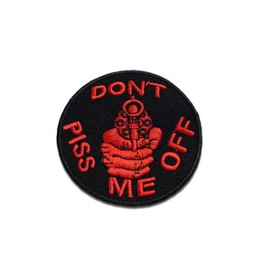 Peut inclure: Un écusson rond brodé noir avec du texte rouge et un dessin rouge d'une main tenant une arme à feu. Le texte se lit "DON'T PISS OFF ME".