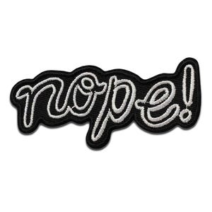 Op de afbeelding: Zwarte strijkpatch met witte geborduurde tekst die "nope!" luidt.