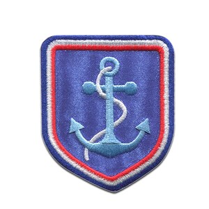 Peut inclure: Écusson brodé bleu avec une ancre bleu clair et une corde blanche. Le patch a une bordure rouge et blanche et une forme de bouclier. Le fond est bleu.