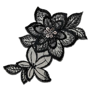 Op de afbeelding: Zwarte kantbloem applicatie met zilveren pailletten in het midden. De applicatie is perfect om een ​​toets van elegantie toe te voegen aan elk project.