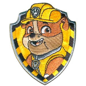 Peut inclure: Patch brodé représentant un chien de dessin animé portant un casque de chantier jaune. Le chien sourit et a un fond rayé noir et jaune. Le patch a la forme d'un bouclier.