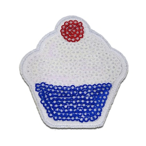 Może przedstawiać: Biały cupcake z niebiesko-białym lukrem i czerwoną wiśnią na górze. Cupcake jest wykonany z cekinów i jest naszywką.