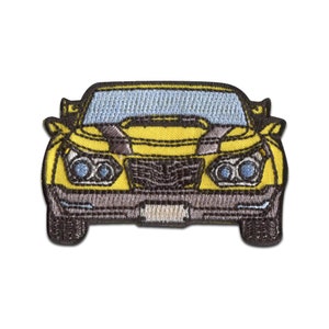 Może przedstawiać: Żółty haftowany znaczek przedstawiający samochód z czarnymi reflektorami i czarną kratką. Samochód jest zwrócony przodem.