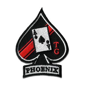 Op de afbeelding: Zwart en wit geborduurde patch in de vorm van een schoppen, met een speelkaart met de Aas van Schoppen. De patch heeft rode accenten en het woord "PHOENIX" aan de onderkant.