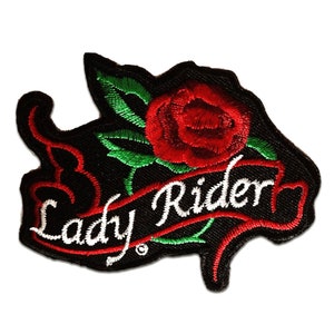 Peut inclure: Écusson brodé avec une rose rouge et des feuilles vertes sur fond noir. Les mots "Lady Rider" sont brodés en blanc sur une bannière rouge. Le patch présente un design détaillé et texturé.