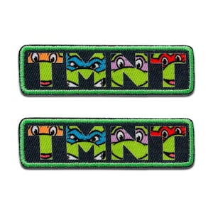 Op de afbeelding: Twee rechthoekige patches met de tekst "TMNT", waarbij elke letter is ontworpen als een Teenage Mutant Ninja Turtle-gezicht. De patches hebben een zwarte achtergrond, groene letters en een groene rand.