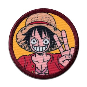 May include: Round embroidered patch featuring a cartoon character with a straw hat, red shirt, and black hair. The character is smiling and giving a peace sign. The patch has a yellow background and a maroon border.