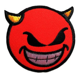 Puede incluir: Un parche bordado rojo con la imagen de una cara de diablo con ojos negros, una amplia sonrisa y cuernos amarillos. El parche tiene un borde negro y una textura cosida, adecuado para aplicar en ropa o accesorios.