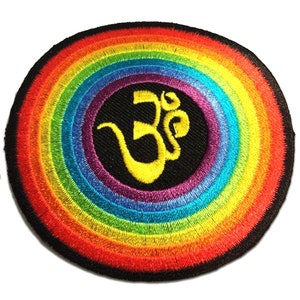Puede incluir: Un parche redondo bordado con un diseño de arcoíris y un símbolo Om en el centro. El símbolo Om es amarillo y el arcoíris está formado por rojo, naranja, amarillo, verde, azul, añil y violeta.