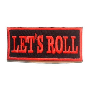 May include: A rectangular patch with the phrase "LET'S ROLL" embroidered in red thread on a black background. The patch has a red border, and the text is in a bold, sans-serif font.
