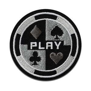 Pode incluir: Etiqueta bordada preta e branca com um design de ficha de cassino. A ficha tem quatro naipes de cartas de jogo no centro e a palavra "PLAY" em letras brancas.
