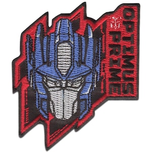 Peut inclure: Écusson brodé représentant le visage d'Optimus Prime en bleu, argent et blanc, sur un fond rouge et noir. Le nom "OPTIMUS PRIME" est affiché verticalement en rouge.