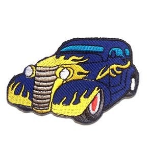 May include: Embroidered patch of a classic hot rod car in navy blue with yellow flames. The car has a light blue roof and a red and white tire. The patch is on a white background.