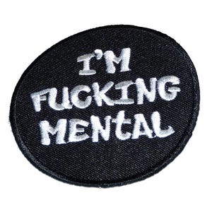 Könnte beinhalten: Schwarzer ovaler Aufnäher mit weiß gesticktem Text „I'M FUCKING MENTAL“. Der Aufnäher hat einen schwarzen Stoffhintergrund und einen weißen Rand. Der Text ist in einer fetten, serifenlosen Schriftart.