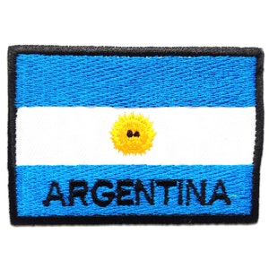 Op de afbeelding: Geborduurde patch met de Argentijnse vlag. Het ontwerp omvat een lichtblauwe achtergrond, een witte middenstreep, een gele zon en het woord 'ARGENTINA' in zwart. De patch heeft een zwarte rand.
