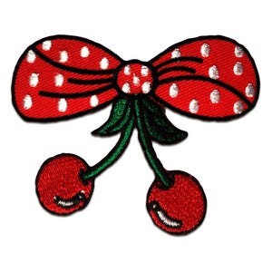 Op de afbeelding: Een rood geborduurde patch met een strik met witte stippen en twee kersen. De kersen zijn rood met groene stelen en lachende gezichten. De patch is ontworpen voor kleding of accessoires.