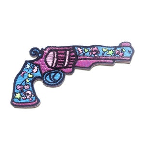 Könnte beinhalten: Ein gestickter Bügeleisen-Aufnäher mit einem Revolver mit Blumen- und Sternmotiven in Pink und Blau.