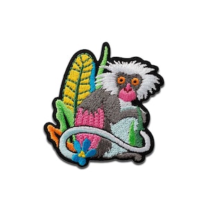 May include: Embroidered patch depicting a monkey with white fur, a grey body, and a pink face. The monkey is surrounded by colourful leaves and a blue flower. The patch has a black border.