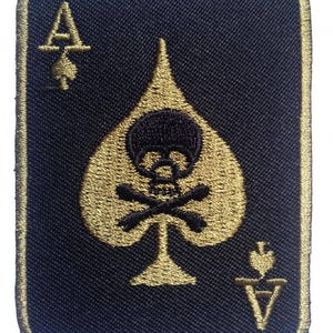 Op de afbeelding: Geborduurde patch in de vorm van een Aas van Schoppen speelkaart. De zwarte kaart heeft een gouden schoppen ontwerp met een doodshoofd en gekruiste botten, en een gouden rand. De kaart heeft ook de letter "A" en een klein schoppensymbool.