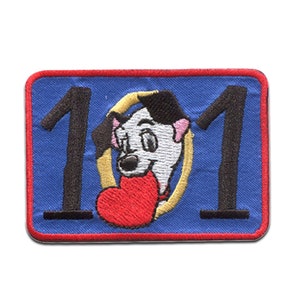 Peut inclure: Patch brodé avec un fond bleu et une bordure rouge. Le patch présente le numéro 101 avec un dessin animé de dalmatien tenant un cœur rouge au centre.