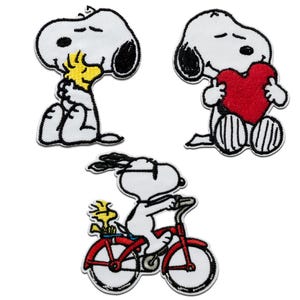 Peut inclure: Ensemble de trois écussons brodés représentant Snoopy et Woodstock. L'un montre Snoopy étreignant Woodstock, un autre tenant un cœur rouge, et le troisième faisant du vélo rouge avec Woodstock. Tous les écussons ont un fond blanc.